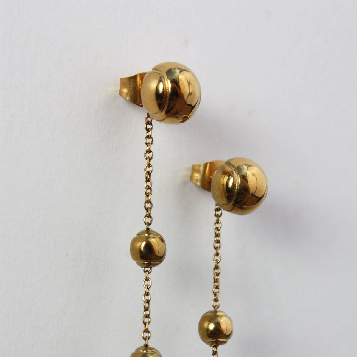 Gold tennis ball stud earrings with delicate chain and smaller gold ball drop accents.