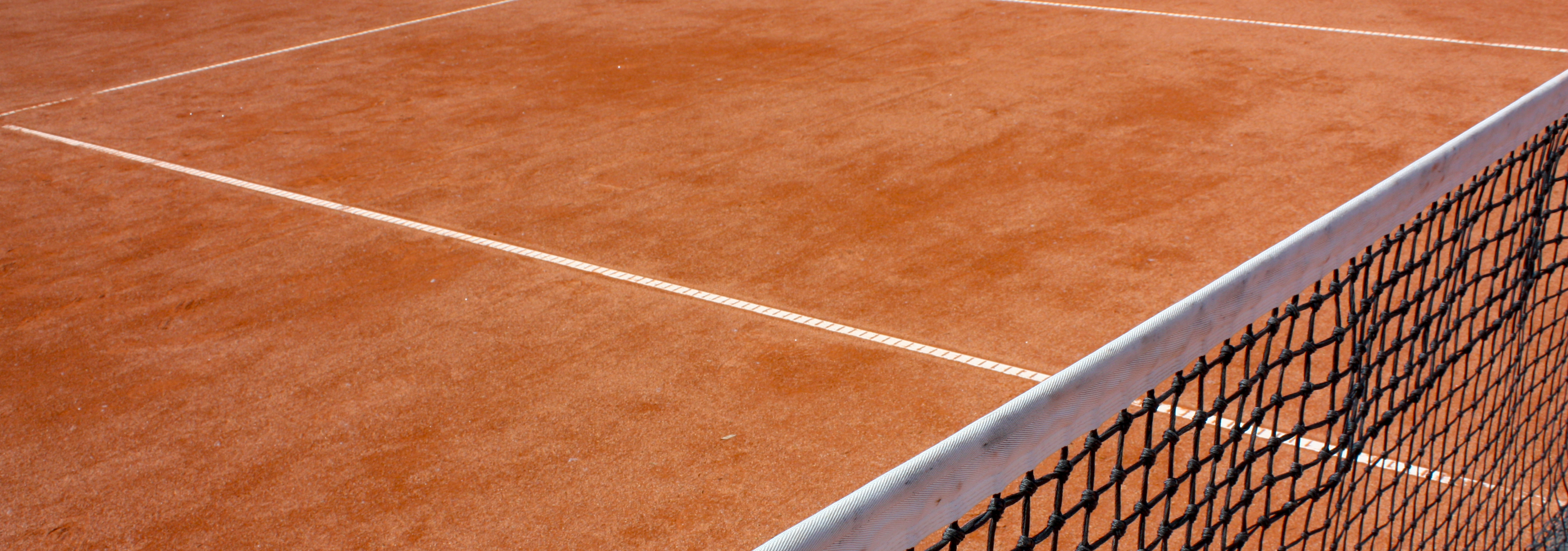 Das Bild zeigt eine Nahaufnahme eines Tennisplatzes. man Sieht das Tennisnetz im Vordergrund und im Hintergrund die Linien des Tennisplatzes.